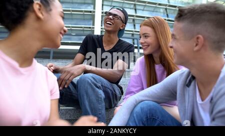 Group of friends laughing sitting school stairs after lessons, teen friendship Stock Photo