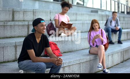 Happy male student sitting campus stairs outdoors, college classmates on break Stock Photo