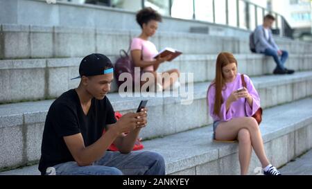 Black male teenager chatting smartphone outdoors, high school students on break Stock Photo
