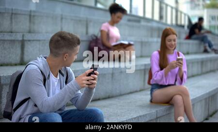 Caucasian millennial with smartphone looking with interest at pretty teenager Stock Photo
