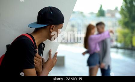 Shocked black teen guy looking girlfriend hugging classmate, unrequited love Stock Photo