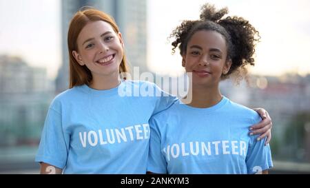 Two female volunteers smiling on camera, high school charity program, altruism