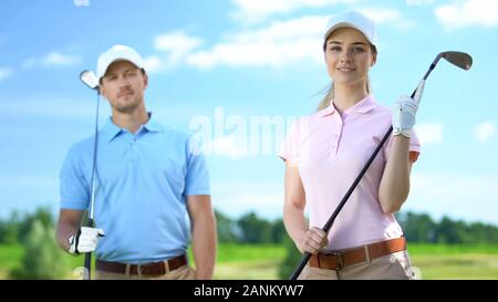 Young female golfer with partner holding clubs and smiling on camera, recreation Stock Photo