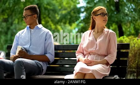 Teen boy and girl ignoring each other sitting on bench in park, failed date Stock Photo