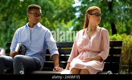 Couple touching hands, sitting on bench in park, reconciliation after quarrel Stock Photo