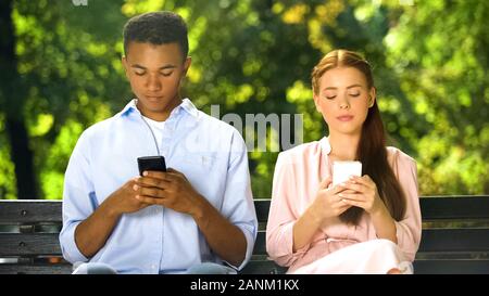 Mixed-race boy making compliment to gadget-addicted girl in social network, fail Stock Photo