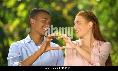 Multiethnic couple making hand heart gesture outdoor, first relations, love Stock Photo
