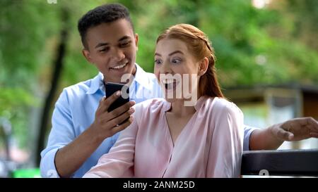 Teen boy showing smartphone screen happy girlfriend, surprise for anniversary Stock Photo
