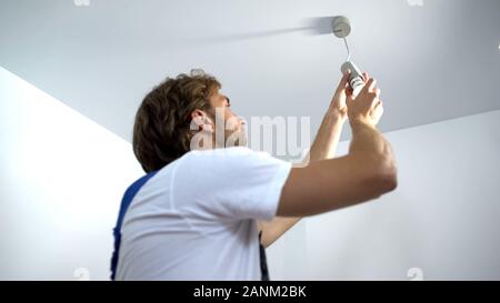 Professional electrician twisting bulb installing light in apartment, service Stock Photo