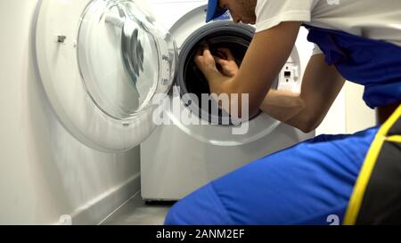 Foreman in uniform repairing washing machine using screwdriver, maintenance Stock Photo