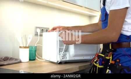 Man in uniform repairing microwave using screwdriver, maintenance guarantee Stock Photo