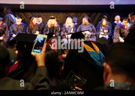 New York, NY / USA - December 13, 2019: Grad garbed in cap and gown takes a seat before the faculty and in front of the crowd of parents as the audien Stock Photo