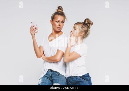 Blonde surprised mom and daughter in white t-shirts and jeans using mobile phones gadgets concept isolated on the white background Stock Photo