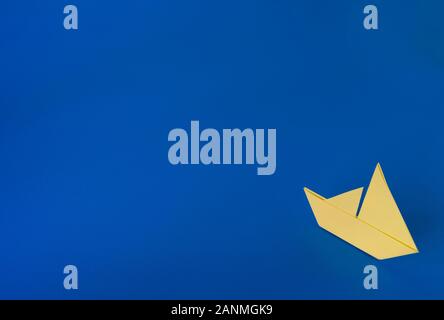 Yellow origami boat against a blue painted background Stock Photo