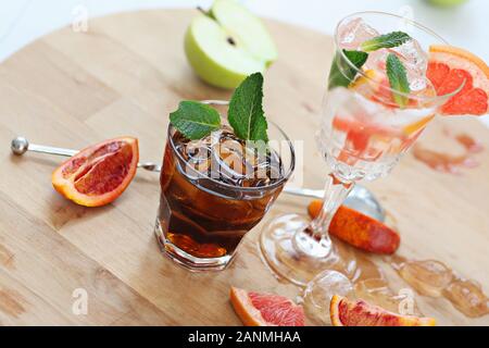 Two cocktails of whiskey with cola and grapefruit with ice vodka and mint. On a wooden board, fragments of fruit are flung up. Photo with depth of Stock Photo