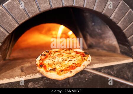 Baked tasty margherita pizza in Traditional wood oven in Naples restaurant, Italy. Original neapolitan pizza. Red hot coal. Stock Photo