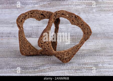 Two rye bread slices with carved holes of heart shape in them on old wooden grey table. Healthy leavened bread. Valentine's or mother's day concept. C Stock Photo