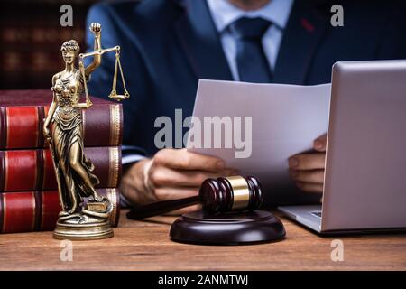 Midsection Of Lawyer Reading Documents Near Mallet And Laptop At Desk In Courtroom Stock Photo