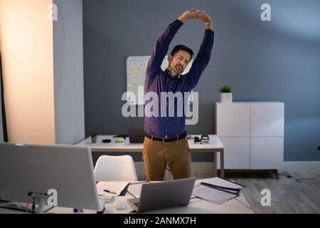 Young Businessman Doing Stretching Exercise In Office Stock Photo