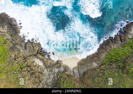 Stunning aerial view of an hidden beach bathed by a turquoise sea and flanked by a green rocky cliff. Lombok Island, West Nusa Tenggara, Indonesia. Stock Photo