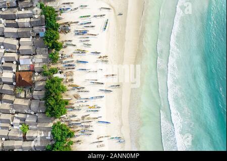 View from above, stunning aerial view of a fishing village with houses and boats on a white sand beach bathed by a beautiful turquoise sea. Stock Photo