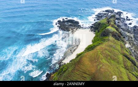 Stunning aerial view of an hidden beach bathed by a turquoise sea and flanked by a green rocky cliff. Lombok Island, West Nusa Tenggara, Indonesia. Stock Photo
