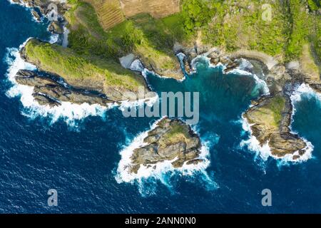 View from above, stunning aerial view of a green rocky cliff bathed by a rough sea during sunset. Lombok Island, West Nusa Tenggara, Indonesia. Stock Photo