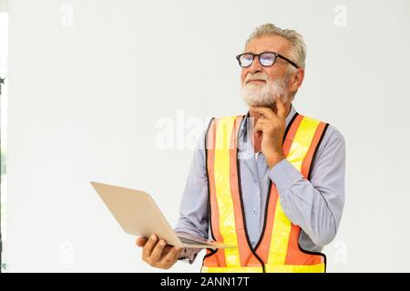 Experienced senior foreman or engineer using laptop computer standing against white background. Construction and engineering concept. Stock Photo