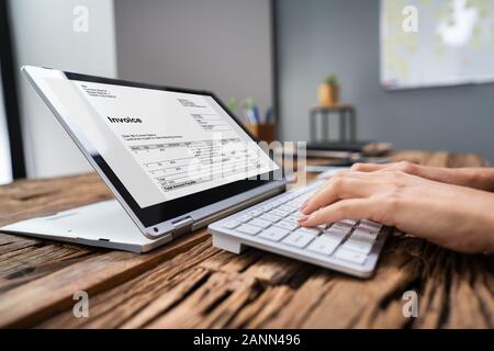 Close-up Of A Businessperson's Hand Analyzing Invoice On Laptop At Workplace Stock Photo