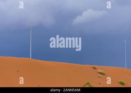 Desert storm clouds contrasted with bold burnt orange colored sand and flooded waters on the sand highlighted green flora and fauna after a storm on t Stock Photo
