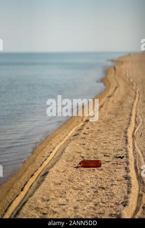 Empty plastic bottle lying on the beach. Environmental pollution. Tire tracks on the sand Stock Photo
