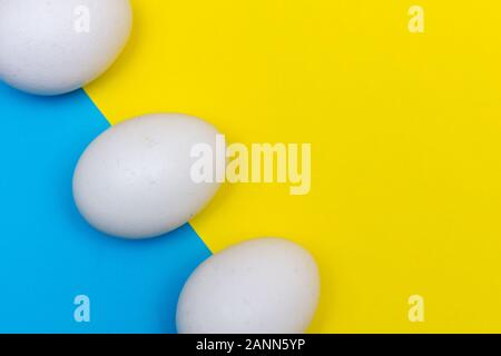 Three Easter holiday flat lay with white egg on a solid bright blue and yellow vibrant background with copy space close up. Stock Photo
