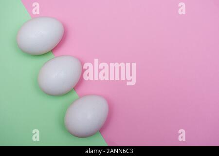Three Easter holiday flat lay with white egg on a solid light green and pink pastel background with copy space. Stock Photo
