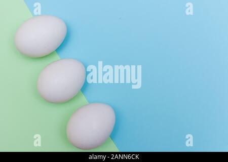 Three Easter holiday flat lay with white egg on a solid light green and blue pastel background with copy space. Stock Photo