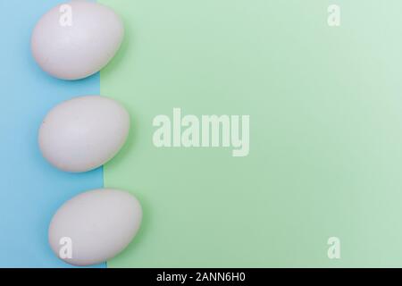Three Easter holiday flat lay with white egg on a solid light green over blue pastel background with copy space. Stock Photo