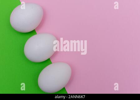 Three Easter holiday flat lay with white egg on a solid bright green, and light pink pastel background with copy space. Stock Photo