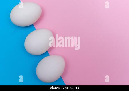 Three Easter holiday flat lay with white egg on a solid bright blue, and light pink pastel background with copy space. Stock Photo