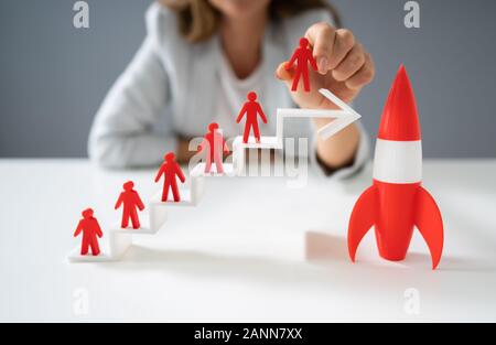 Woman Placing Red Human Figurine Standing On White Increasing Arrow Graph Near Red Rocket Stock Photo