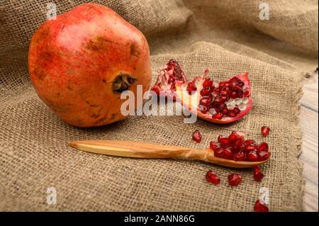 Ripe juicy pomegranate, pieces of pomegranate and pomegranate seeds on a wooden spoon on a background of rough homespun fabric. Close up Stock Photo