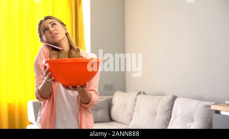 Upset household calling roof repair service while water leaking from ceiling Stock Photo