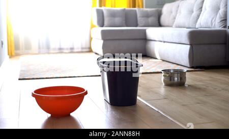 Water dropping in bucket and dishes from ceiling, risk of shingles, damaged roof Stock Photo