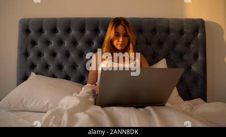 Tired woman working on laptop in bed till morning, overburdened freelancer Stock Photo