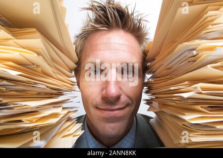 Tired office worker putting on a happy face between two huge stacks of files Stock Photo