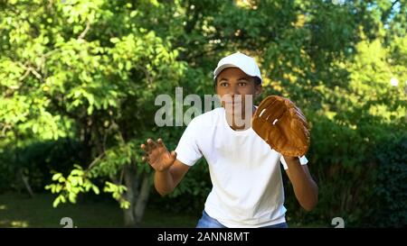 Happy black male teenager wearing white cap receiving baseball, sport and hobby Stock Photo