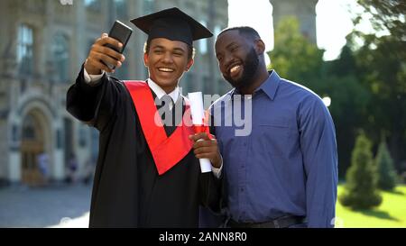 Happy university student graduation mantle and father taking selfie smartphone Stock Photo