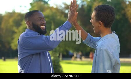Cheerful black brothers giving high five outdoors, happy family, close relations Stock Photo