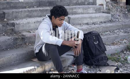 Pensive afro-american teenager with beer bottle sitting on stairs, difficult age Stock Photo