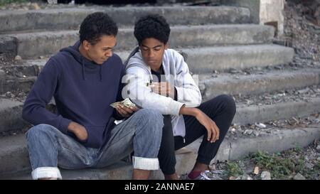 Needy young men counting money sitting stairs, dysfunctional family children Stock Photo