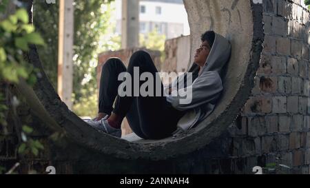 Sad lonely student in hoodie sitting alone abandoned building, puberty isolation Stock Photo