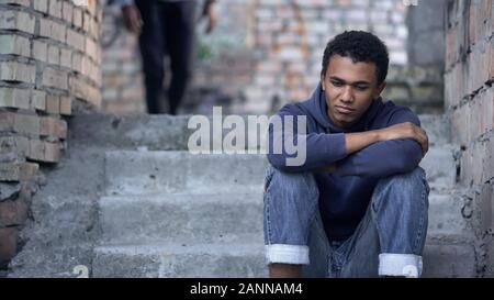 Pensive afro-american teenager sitting on stairs, misunderstanding with parents Stock Photo